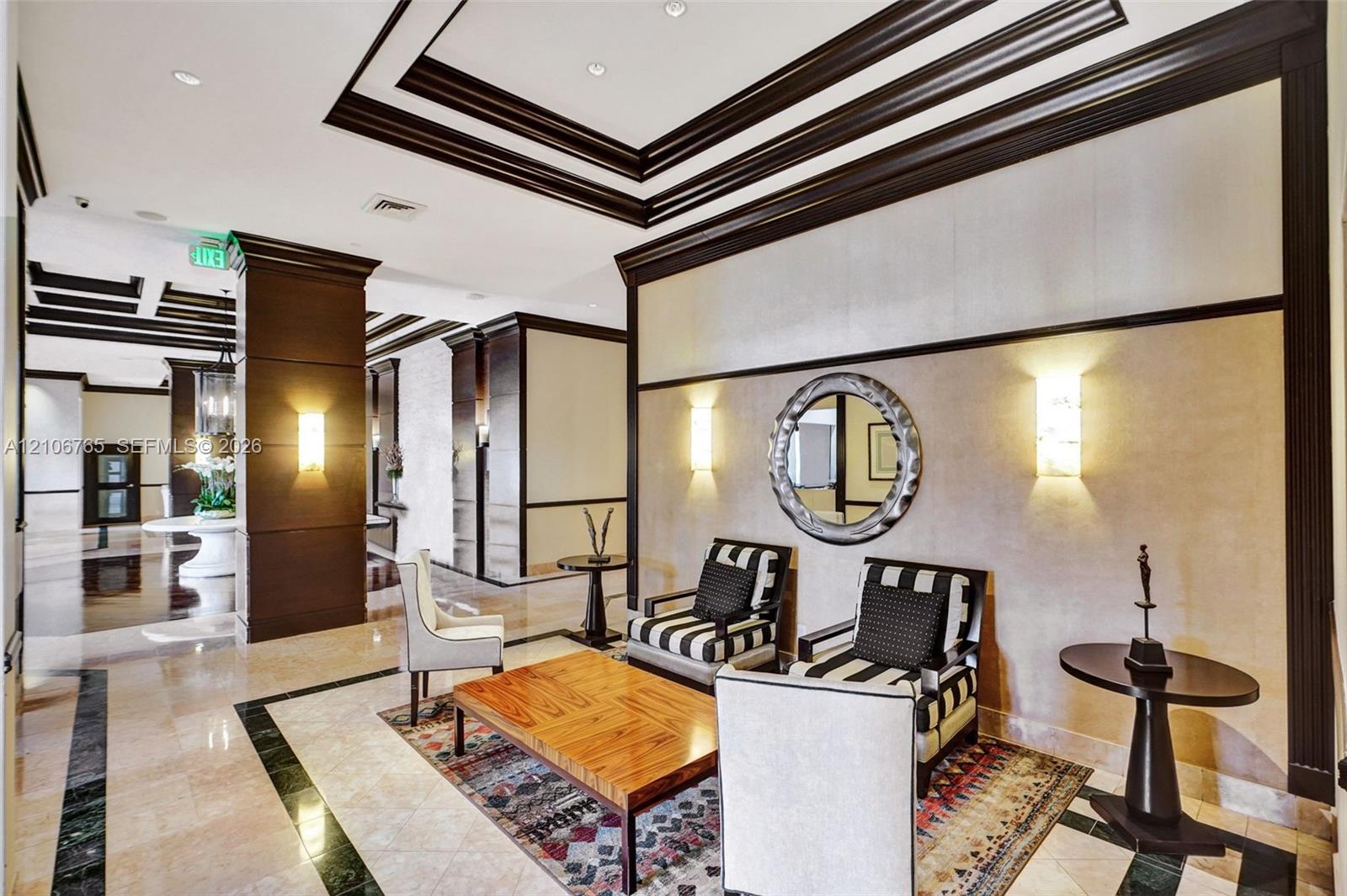 Entryway, multi-tiered crown molding, recessed lighting, stone flooring with decorative dark stone borders, paneled column accents, and wall-mounted sconces.