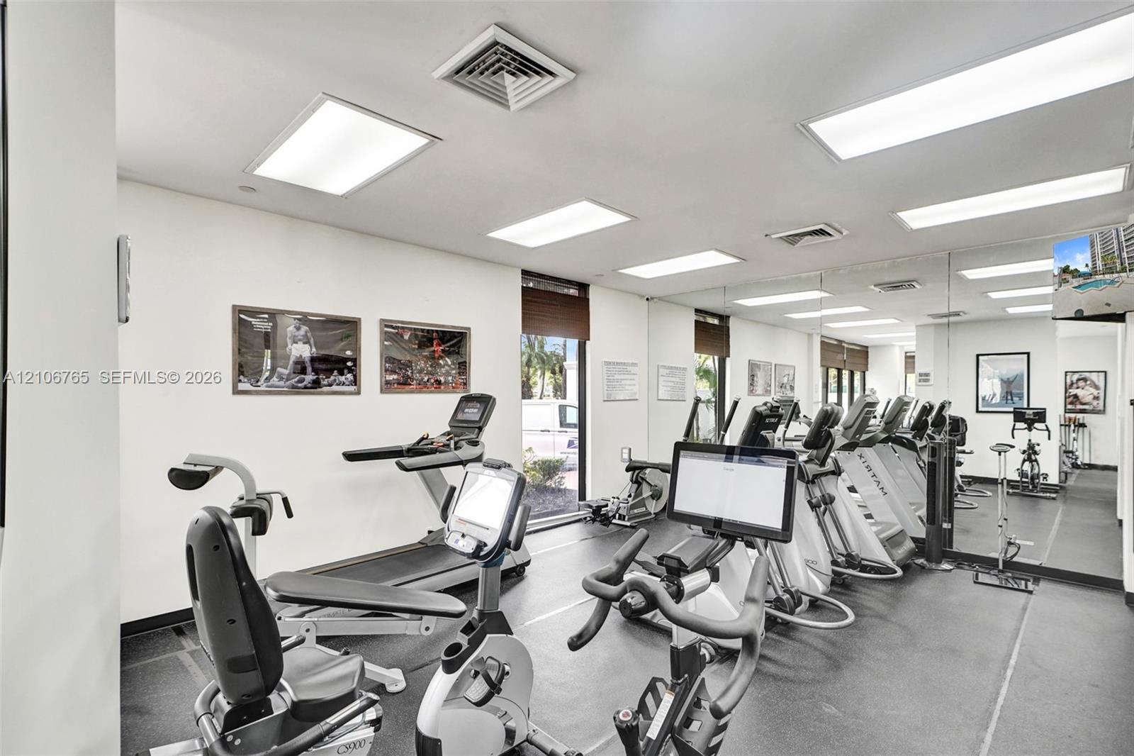 Fitness space, resilient rubber flooring, expansive wall-to-wall mirrors, recessed lighting, and large windows.
