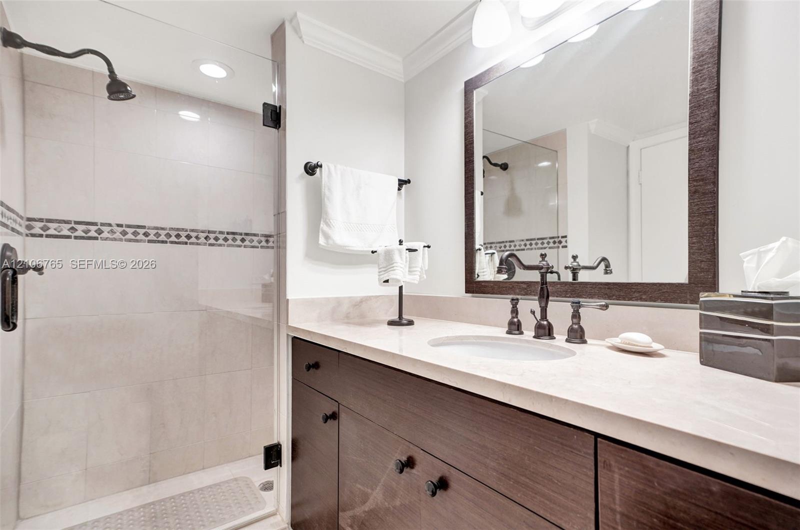 Second bathroom. Custom wood-finish vanity with a stone countertop, under-mount sink, walk-in shower with a glass enclosure and decorative tile inlay.