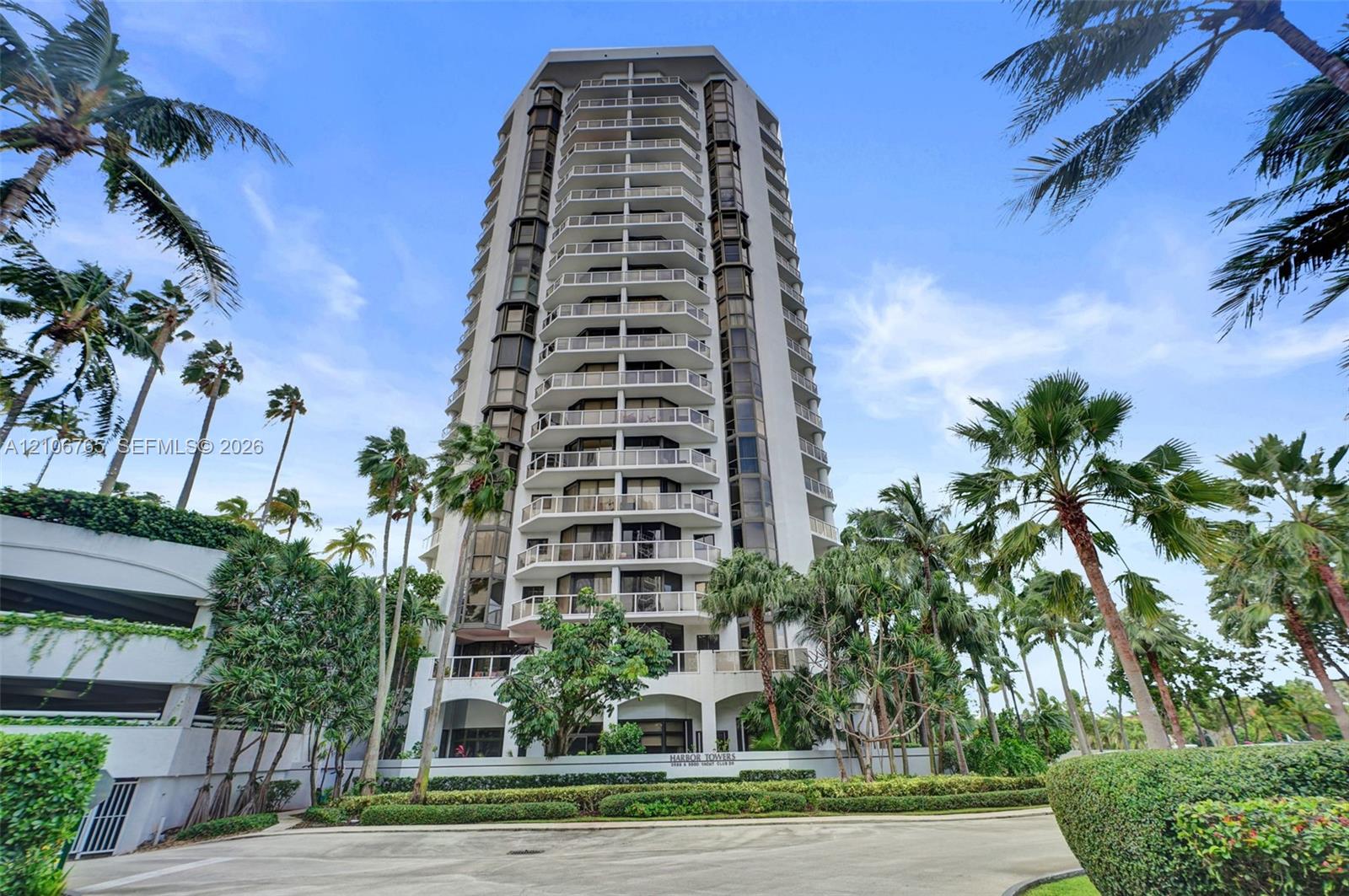High-rise building exterior featuring tiered balconies, expansive glass windows, palm tree landscaping.