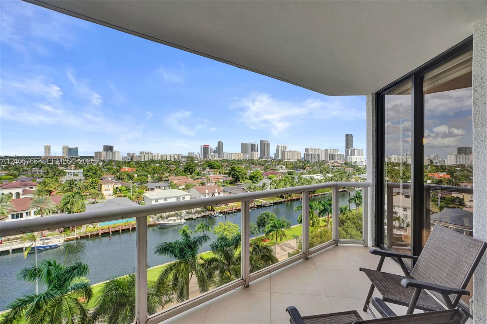 Covered balcony overlooking a canal, tropical landscaping, and a distant city skyline. Covered balcony overlooking a canal, tropical landscaping, and a distant city skyline.