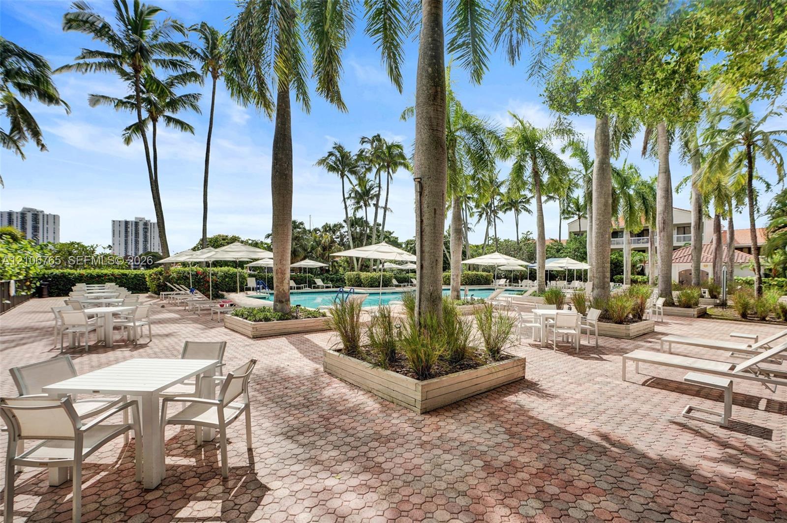 Outdoor terrace featuring brick-paver hardscaping, built-in raised planters, mature palm trees, and a swimming pool