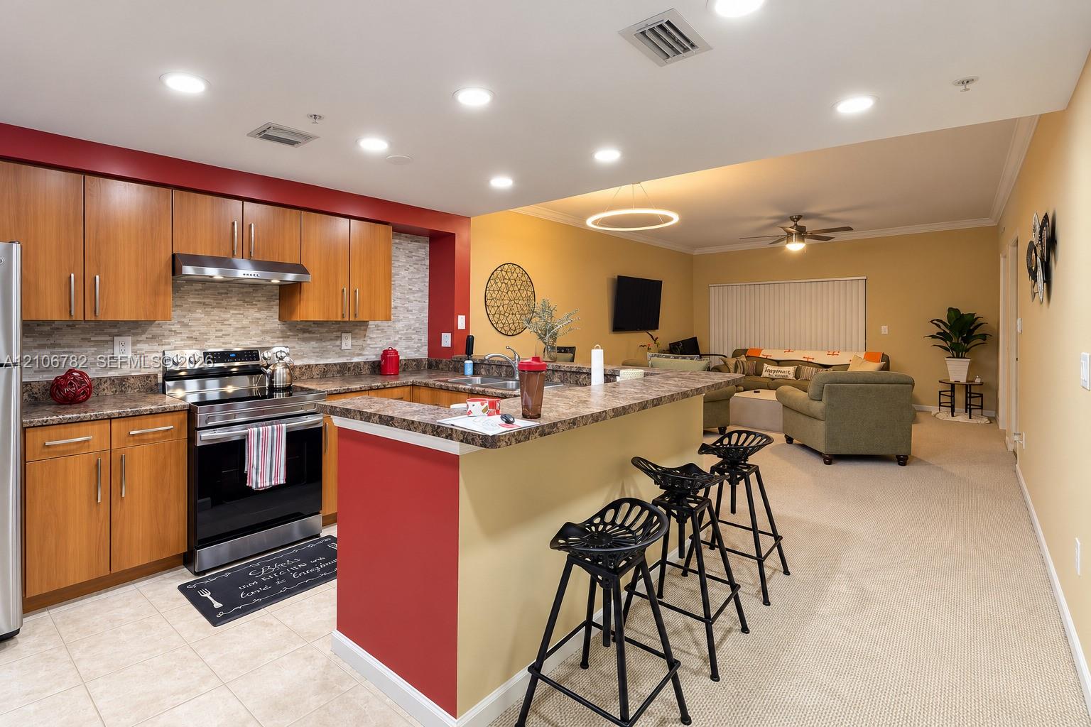 Kitchen featuring wood-finish cabinetry, stone-patterned countertops, a tiled backsplash, built-in stainless steel appliances, and a peninsula breakfast bar