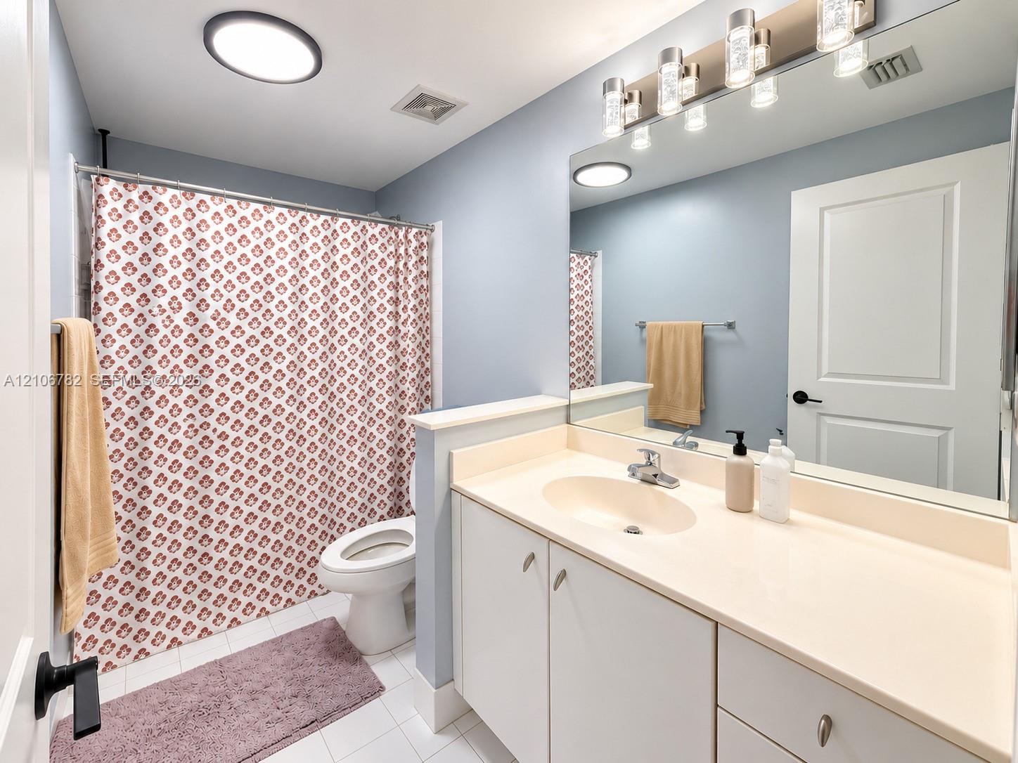 Bathroom featuring a white single-sink vanity with integrated countertop, large wall-mounted mirror, multi-bulb vanity lighting, and a bathtub-shower combination