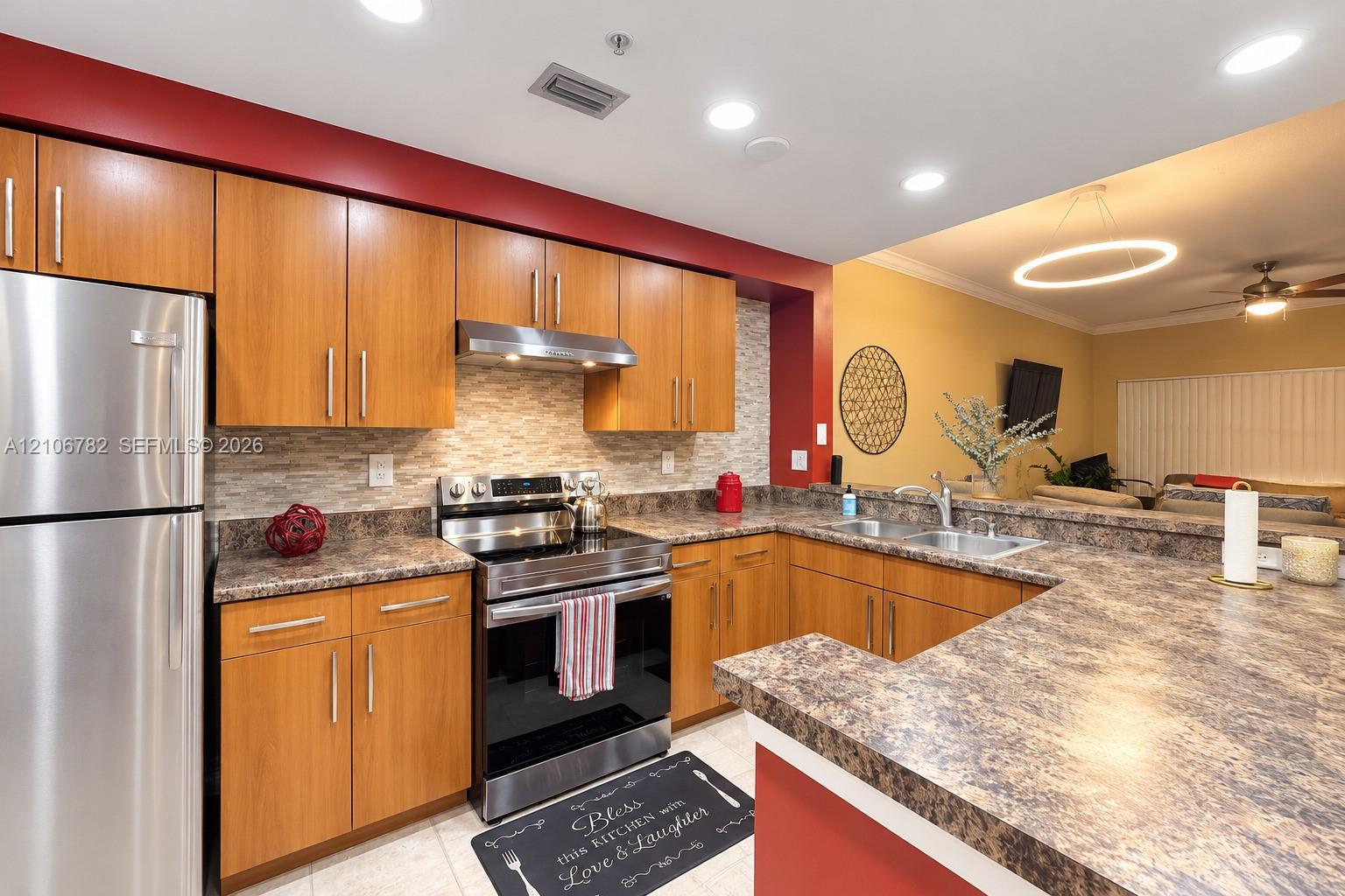 Kitchen featuring wood-finish cabinetry, stone-patterned laminate countertops, stainless steel appliances, a textured stone-tile backsplash, and recessed lighting