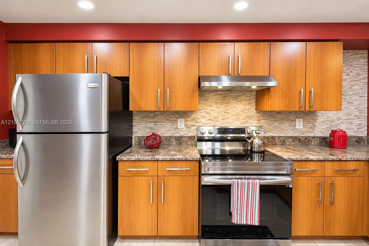 Kitchen featuring wood cabinetry, stainless steel appliances, a textured stone-finish backsplash, laminate countertops, and recessed lighting
