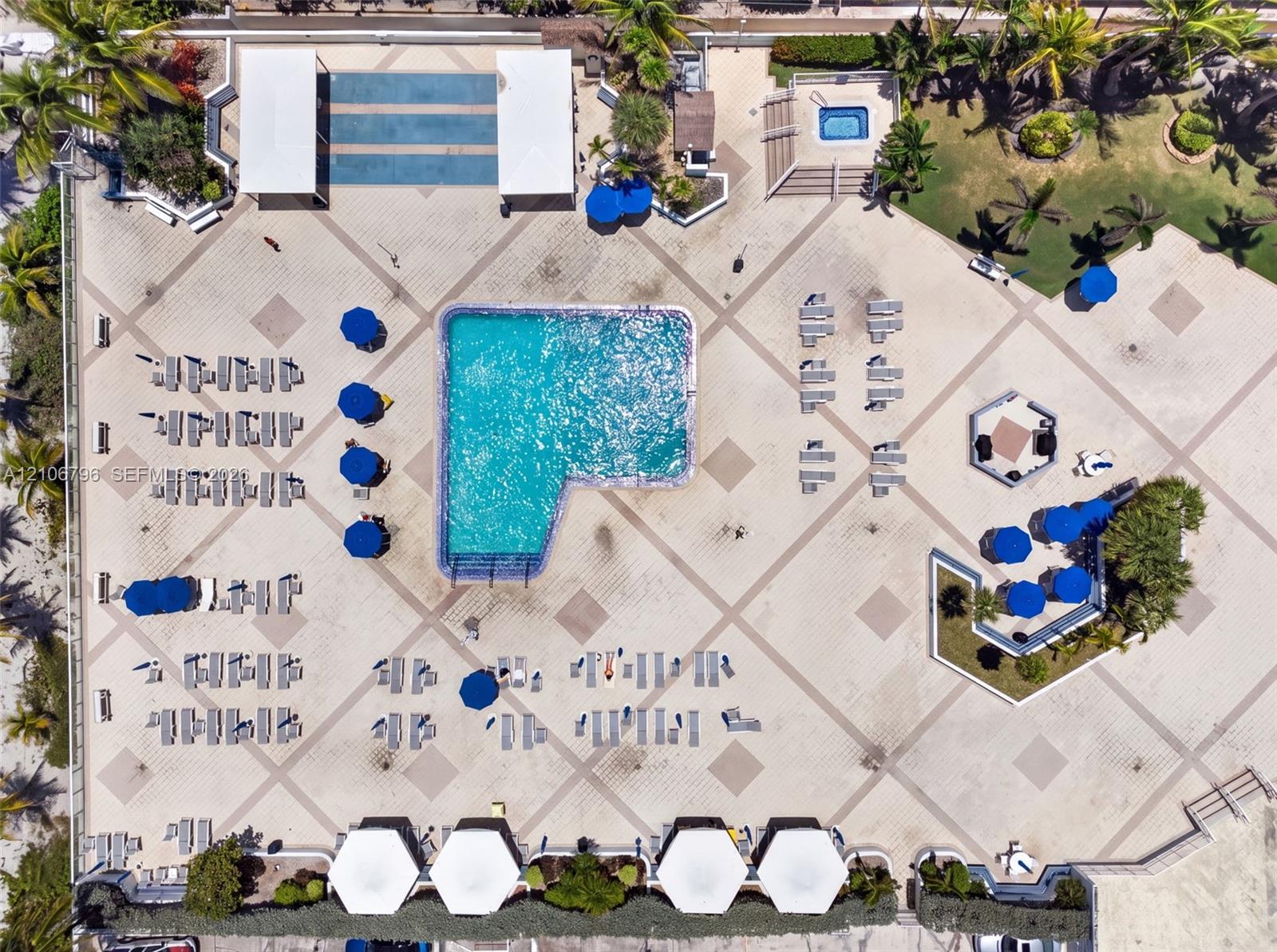 Aerial perspective of a pool area featuring a multi-level swimming pool, an elevated spa, expansive stone-paver decking, and dedicated shaded structures