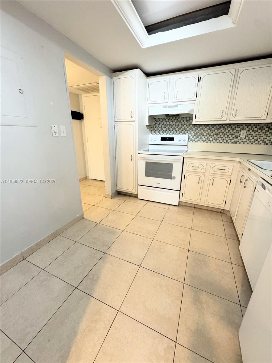 Kitchen featuring white cabinetry, a neutral tile backsplash, built-in range, tile flooring, and a ceiling skylight