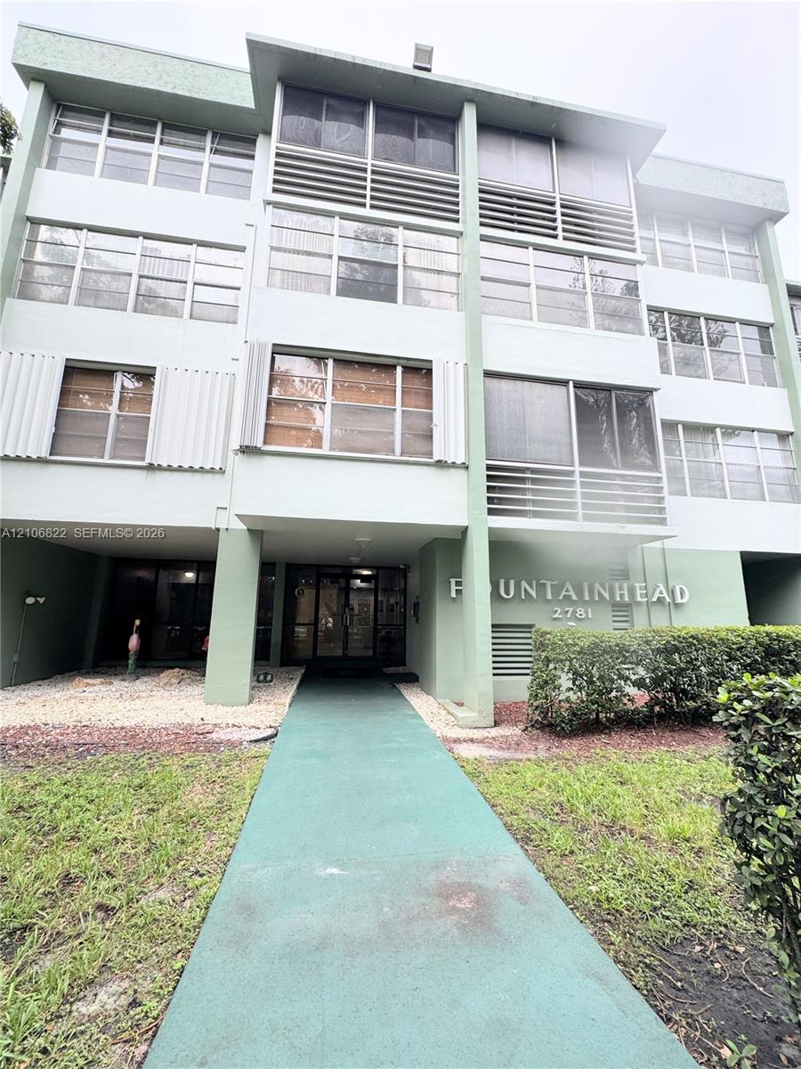 Multi-story residential building exterior featuring a structured facade with integrated balconies, expansive multi-pane window groupings, and a covered ground-level entryway
