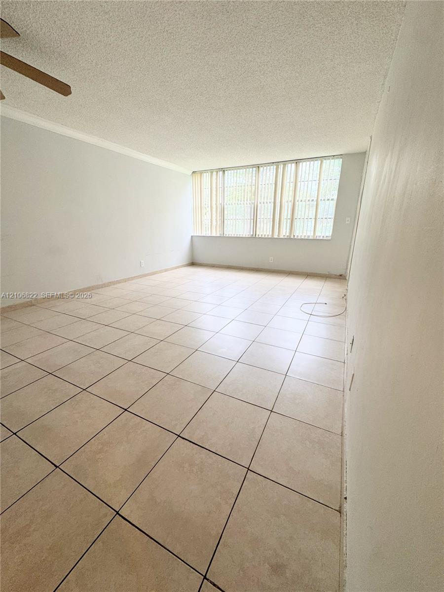 Interior space featuring large-format tile flooring, textured ceiling, and expansive windows with integrated vertical blinds