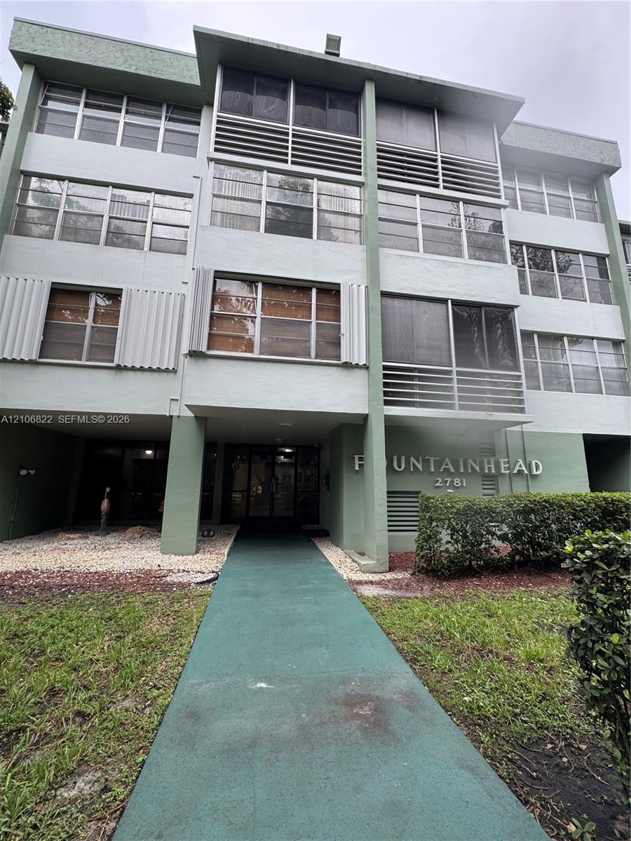 Multi-story residential building exterior featuring a covered entryway, screened balconies, and vertical architectural accents