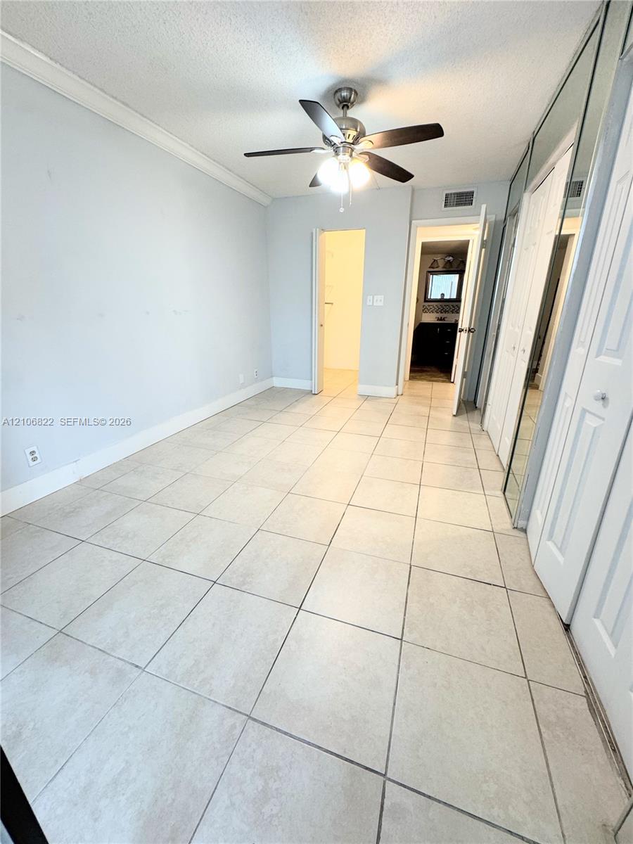 Neutral-toned tile flooring, ceiling fan with integrated light fixture, and floor-to-ceiling mirrored closet doors