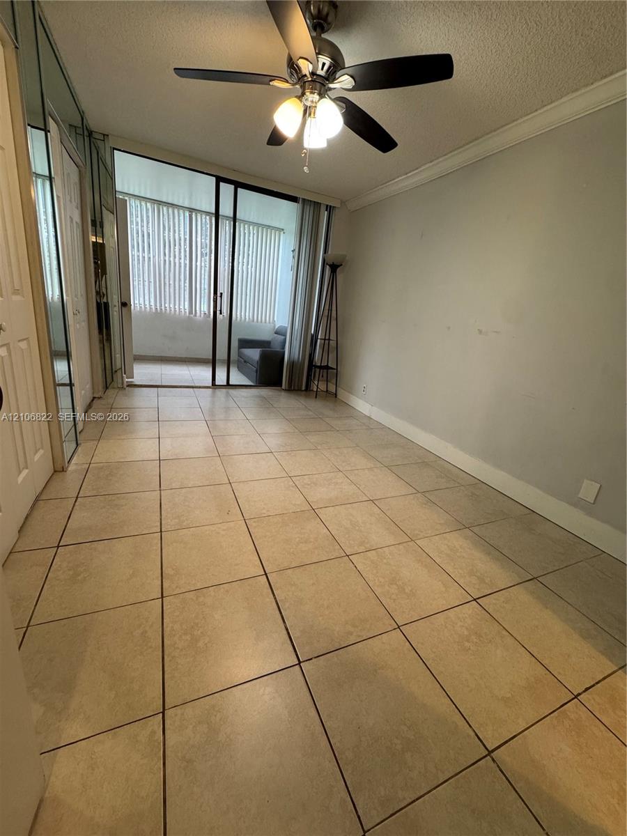 Neutral tile flooring, ceiling fan with light fixture, mirrored sliding closet doors, and glass sliding doors leading to an enclosed balcony