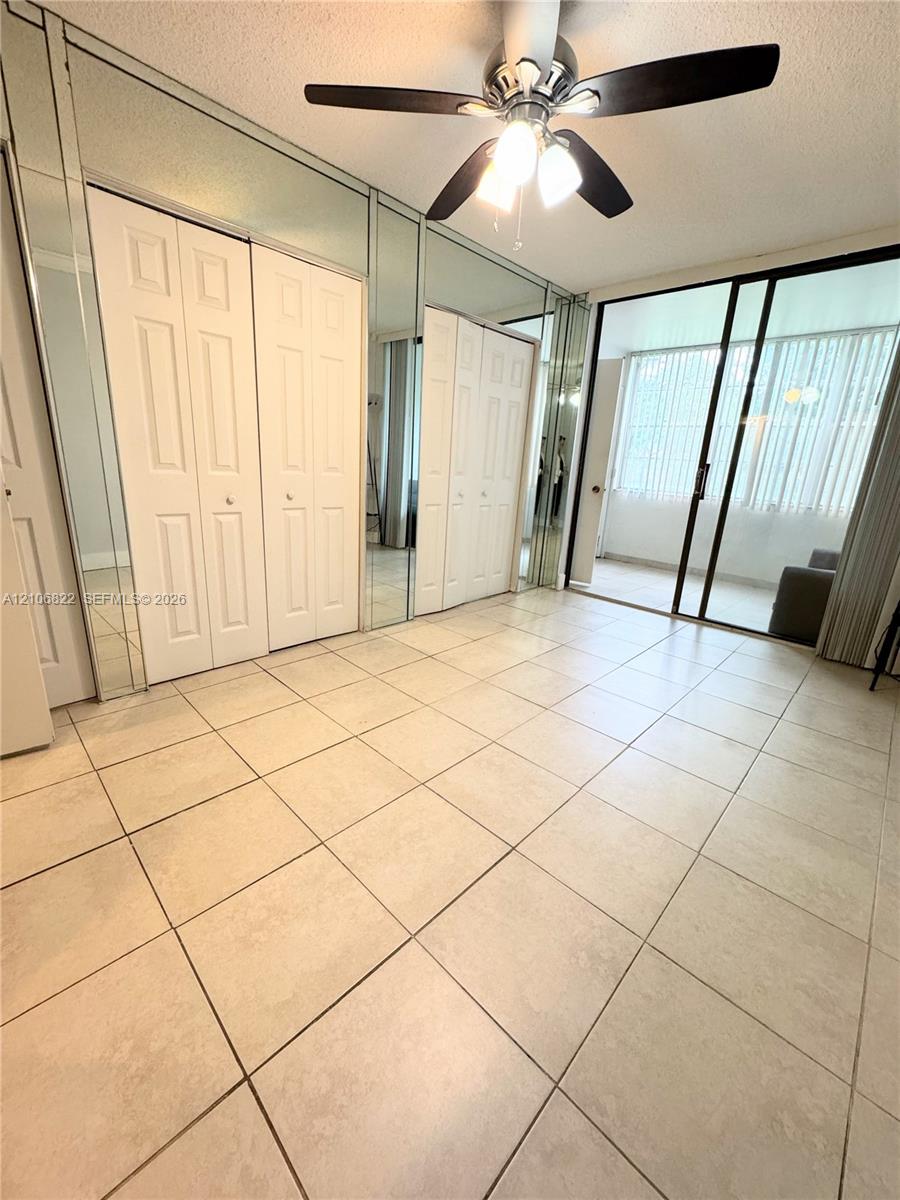 Ceramic tile flooring, floor-to-ceiling mirrored closet doors, and sliding glass patio doors with vertical blinds, finished with a ceiling fan with integrated light fixture