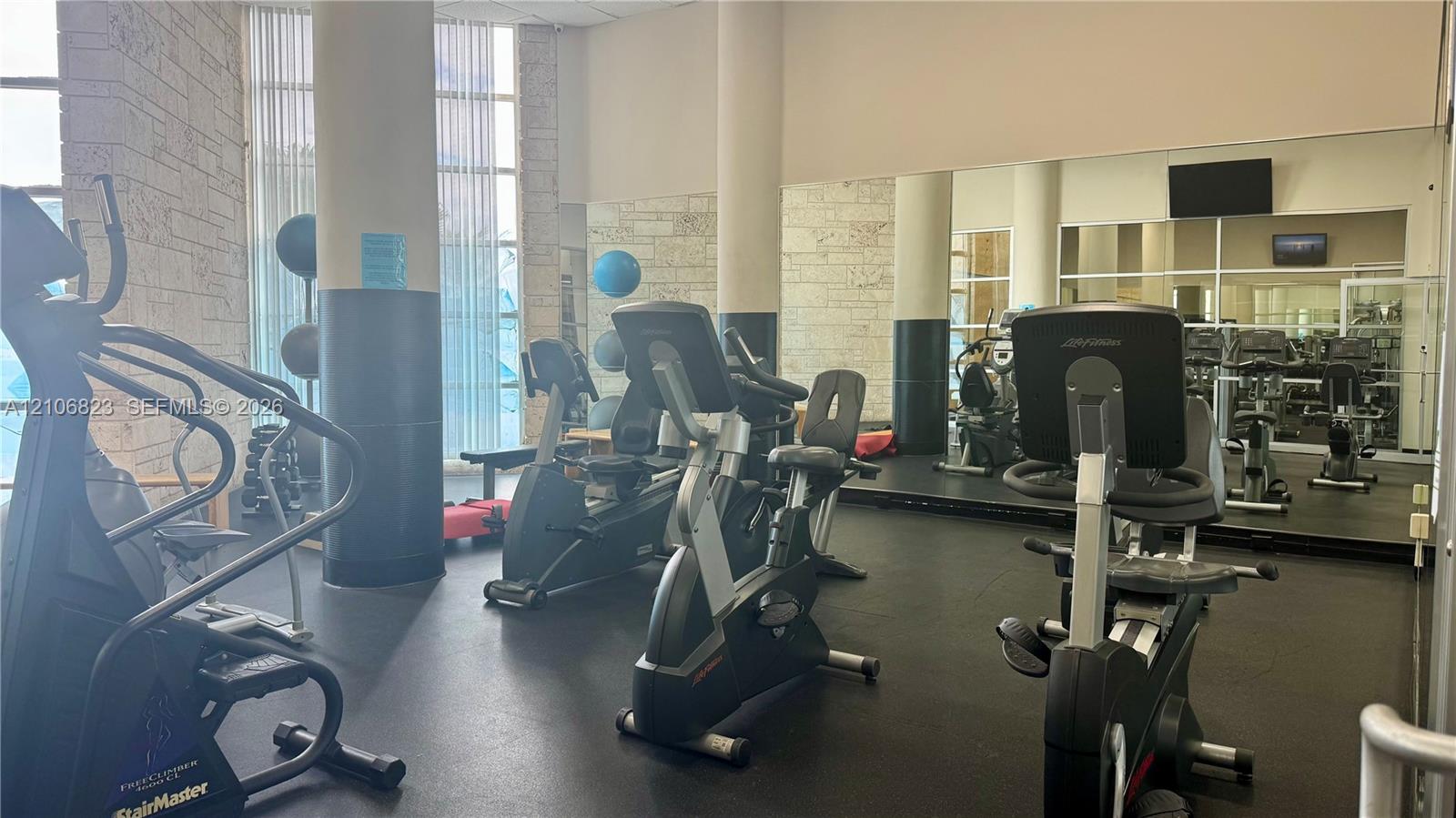 Fitness center featuring floor-to-ceiling windows, natural stone wall accents, full-length wall mirrors, and rubberized flooring