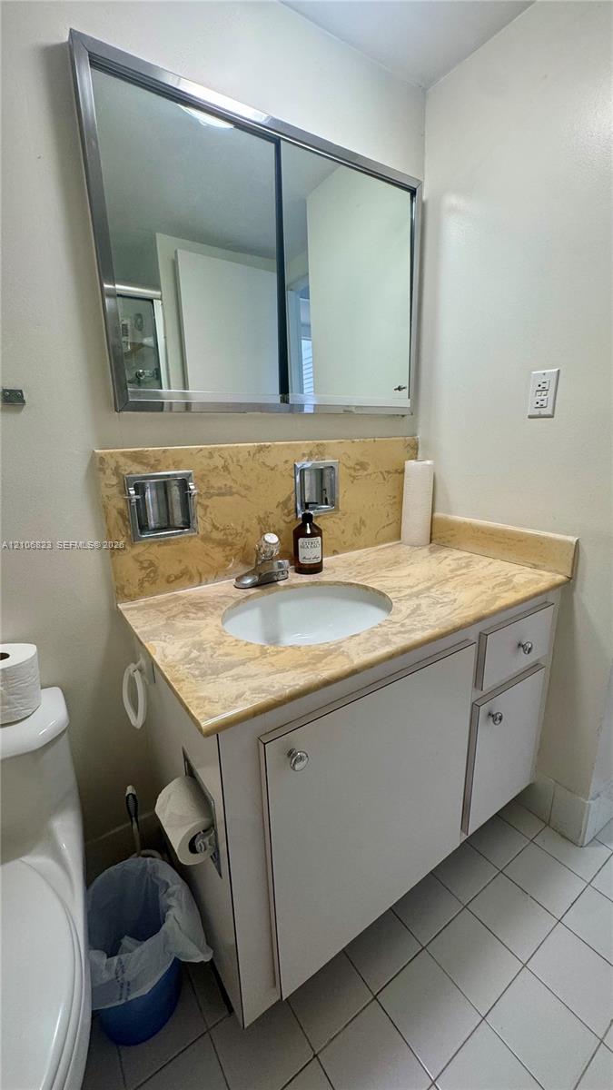 Vanity featuring a stone-patterned countertop, integrated undermount sink, white cabinetry with polished knobs, and a large-format metallic-framed medicine cabinet
