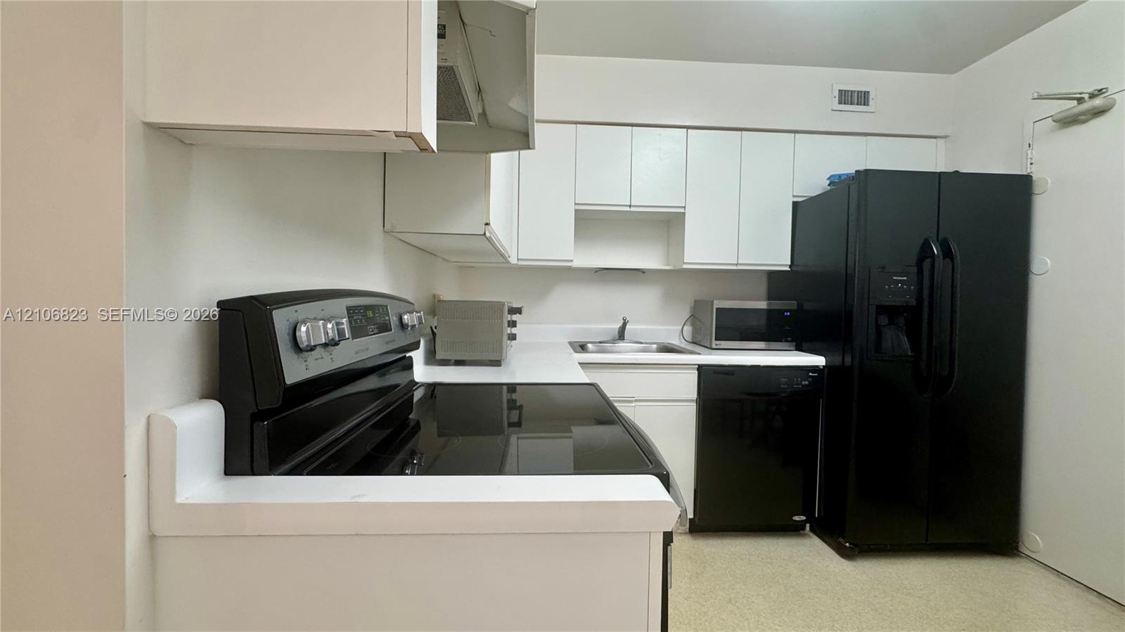 Kitchen featuring white cabinetry, contrasting black appliances, solid-surface countertops, and a dual-basin sink