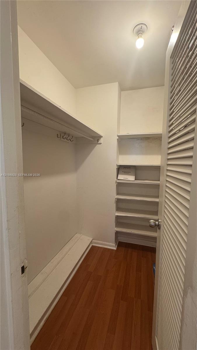 Storage area featuring wood-finish flooring, a built-in hanging rod, multiple fixed shelving units, and a louvered door