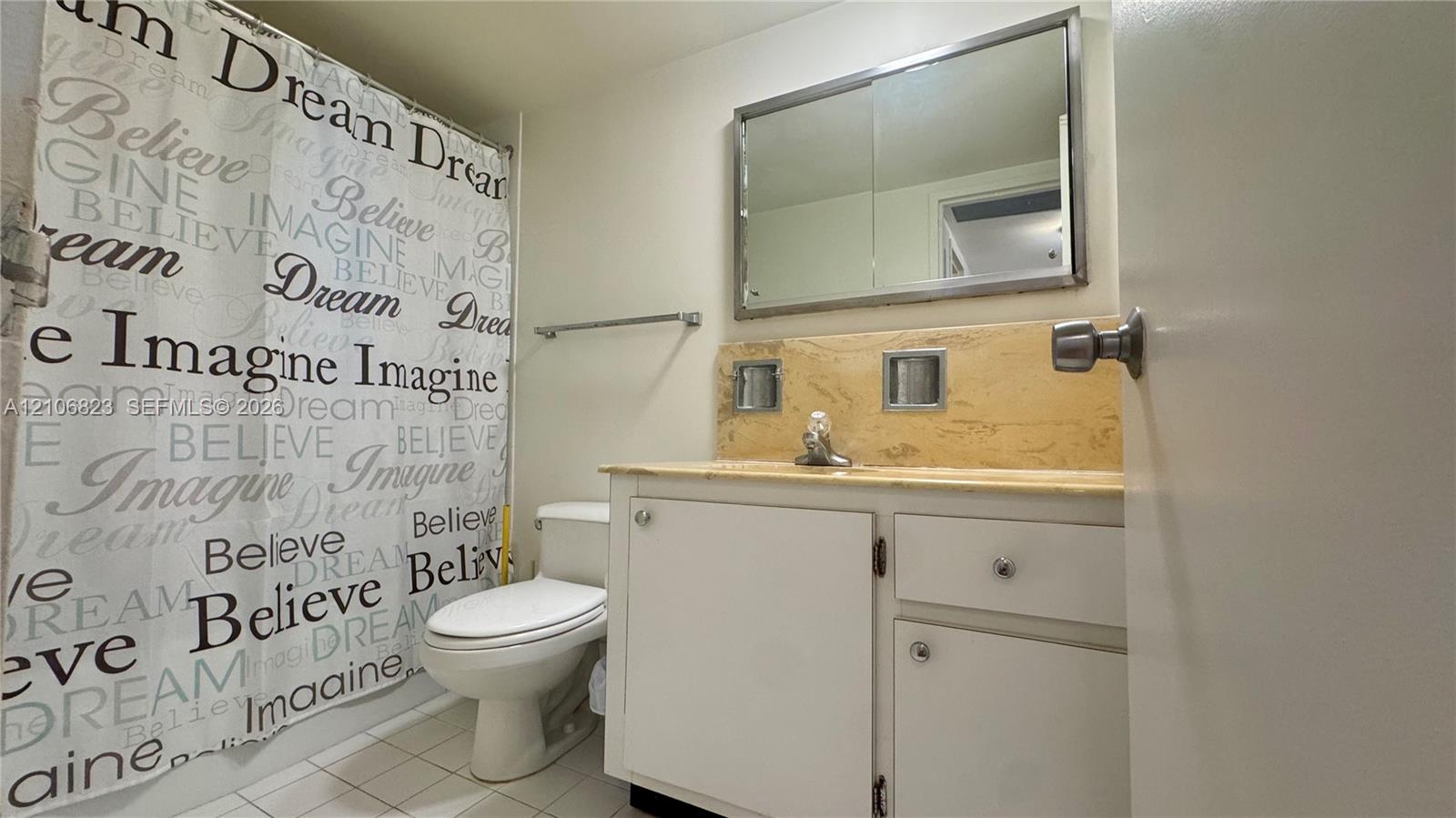 Bathroom featuring a vanity with neutral stone-style countertop, integrated sink, large wall-mounted mirror, and tiled flooring