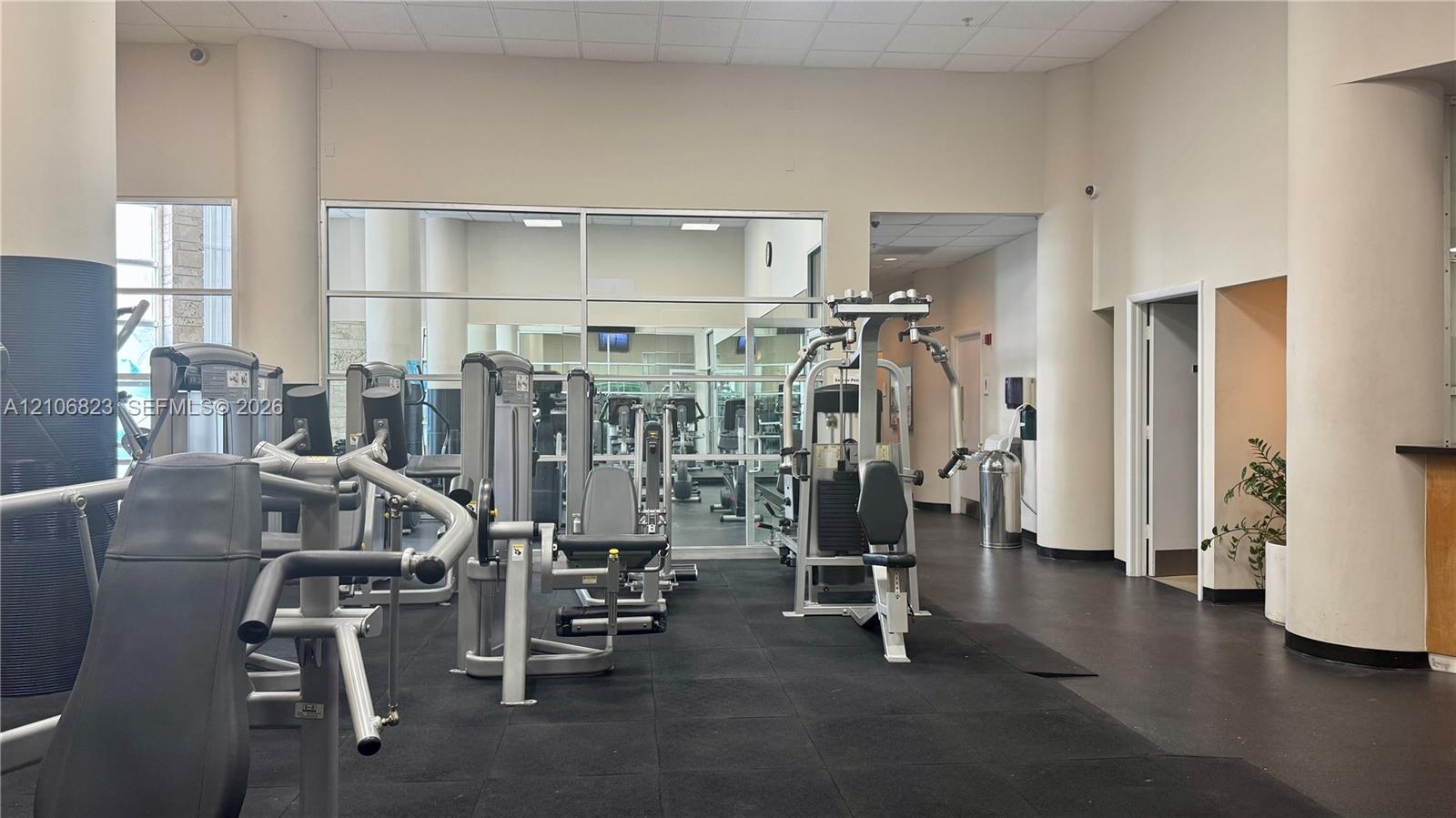 Fitness center featuring rubberized flooring, floor-to-ceiling mirrors, and structural columns