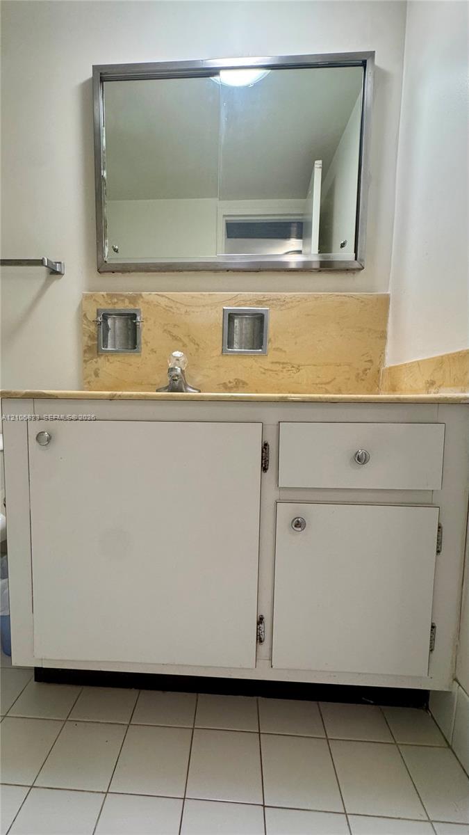 White vanity cabinet with chrome hardware, natural stone countertop with matching backsplash, dual inset soap dishes, and a framed mirror