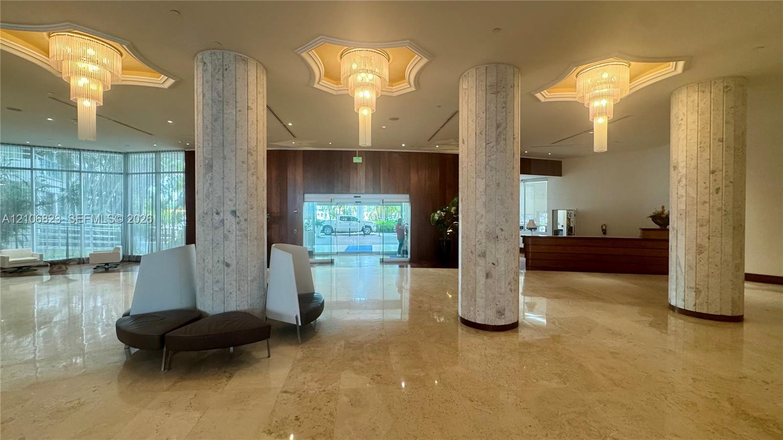 Grand lobby featuring polished stone flooring, three tiered crystal chandeliers, floor-to-ceiling glass windows, custom wood paneling, and stone-clad structural columns