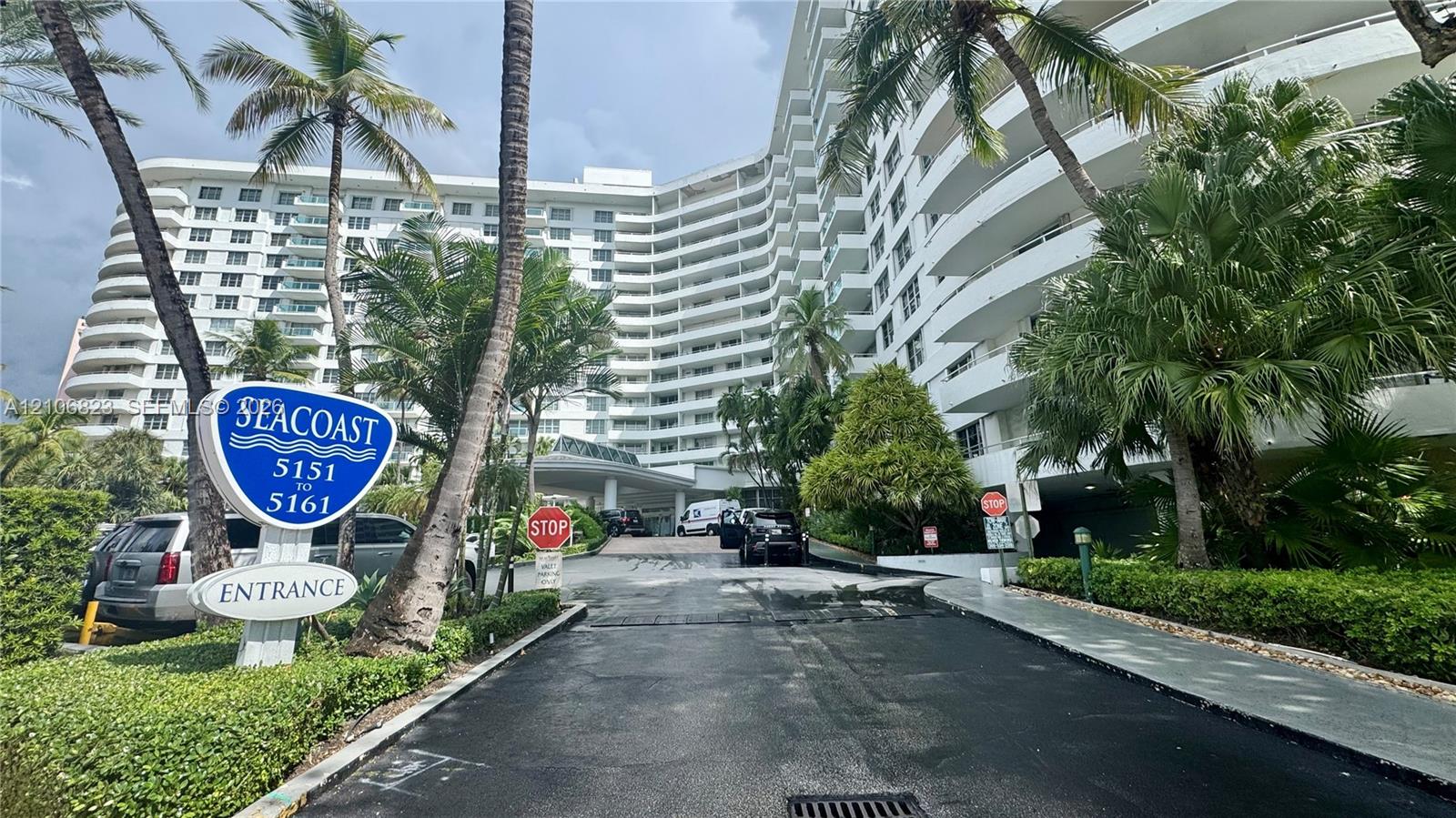 Mid-rise residential building with wrap-around balconies, porte-cochre entrance, and mature tropical landscaping
