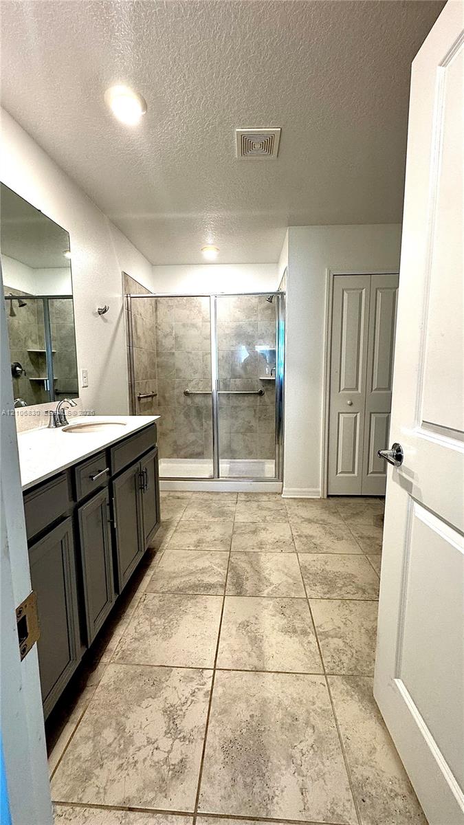 Bathroom featuring a dual-door vanity with a white countertop, walk-in shower with tile surround and glass enclosure, and large-format tile flooring