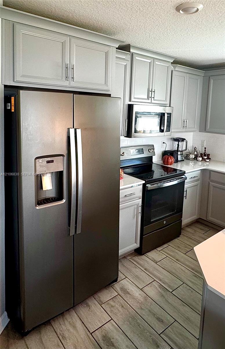 Kitchen featuring shaker-style cabinetry, stainless steel appliances, white solid-surface countertops, and wood-finish tile flooring Kitchen featuring shaker-style cabinetry, stainless steel appliances, white solid-surface countertops, and wood-finish tile flooring