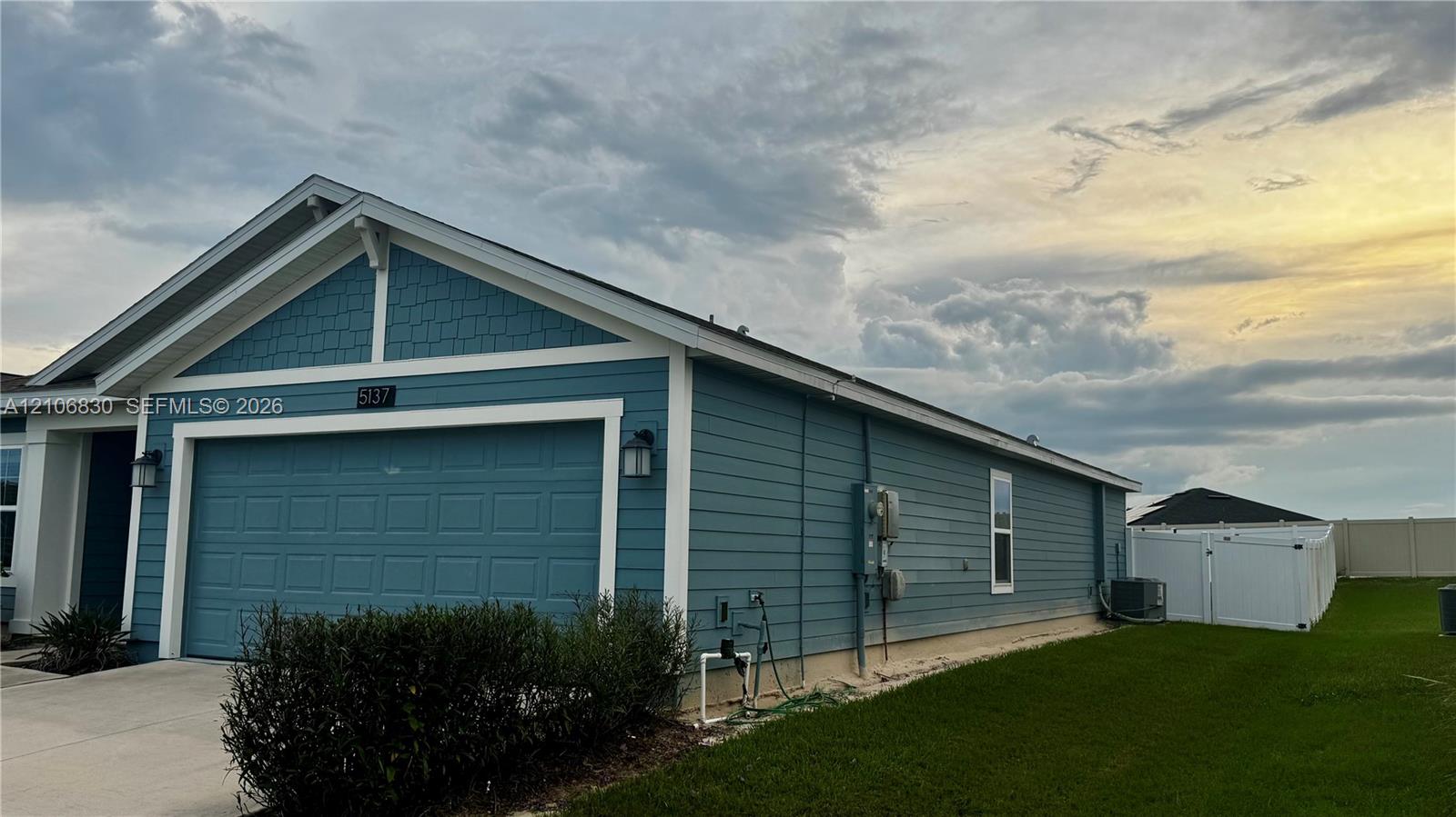 Single-story exterior featuring blue horizontal siding, shingle-style gable detailing, an attached garage, and white vinyl perimeter fencing