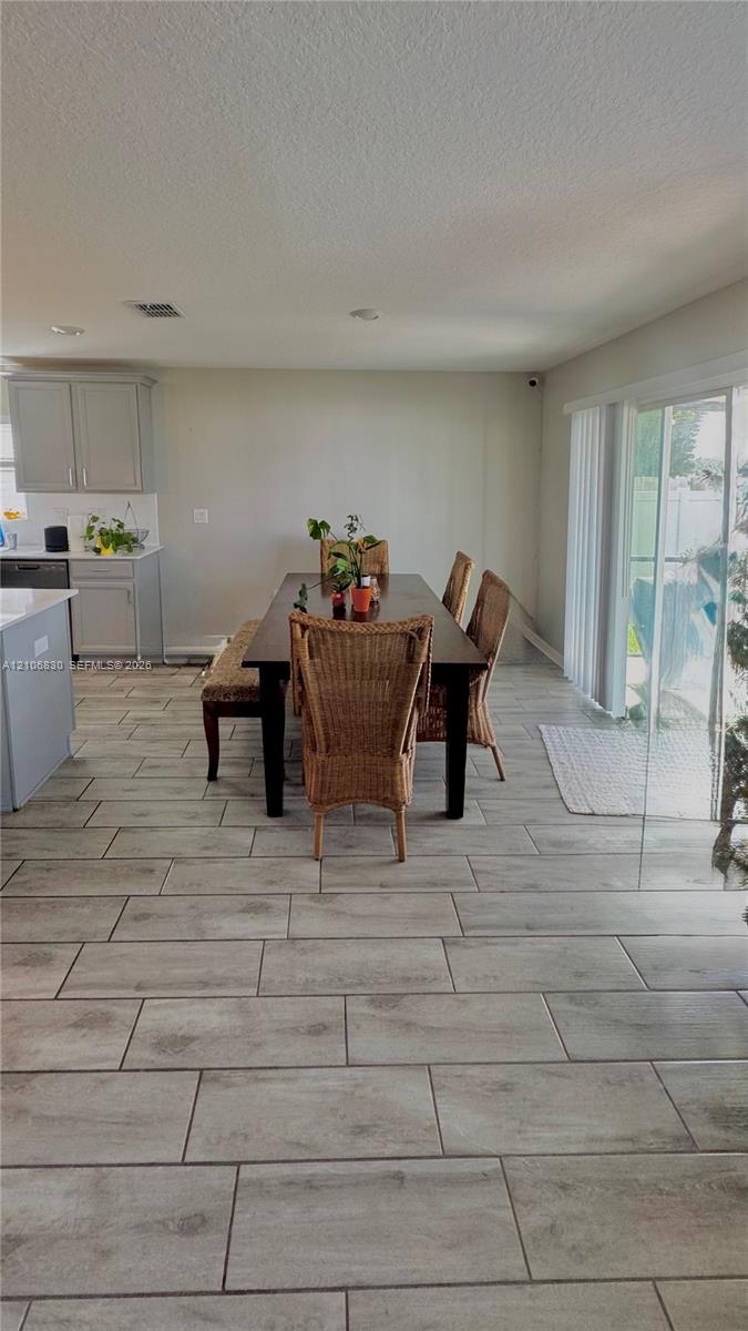 Open-concept interior featuring wood-finish tile flooring, recessed lighting, neutral-toned kitchen cabinetry, and sliding glass doors Open-concept interior featuring wood-finish tile flooring, recessed lighting, neutral-toned kitchen cabinetry, and sliding glass doors