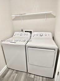 Laundry area featuring a top-loading washing machine, clothes dryer, and wall-mounted white shelving over wood-finish flooring