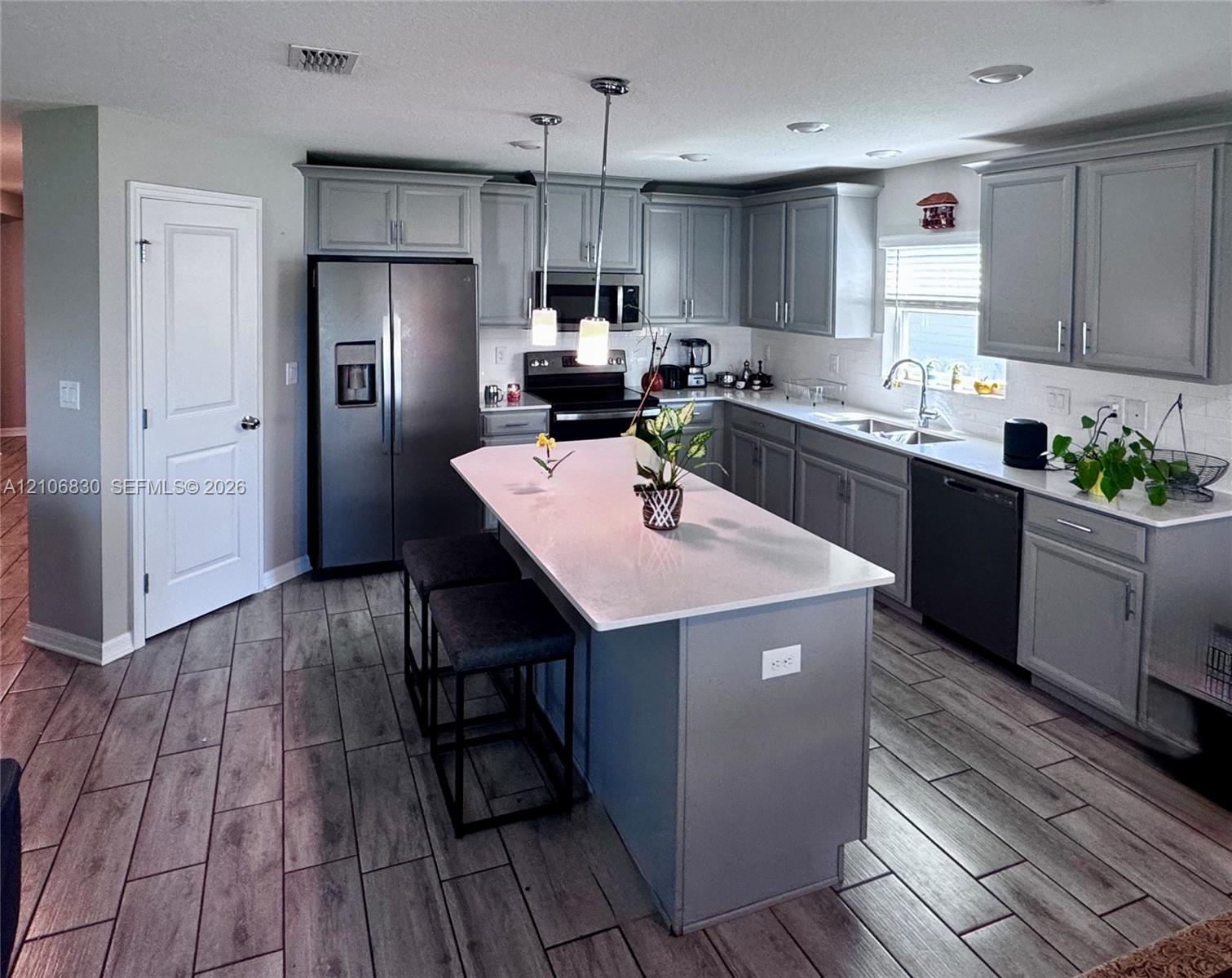 Kitchen featuring gray cabinetry, a central island with a solid surface countertop, wood-finish tile flooring, recessed lighting, and stainless steel appliances Kitchen featuring gray cabinetry, a central island with a solid surface countertop, wood-finish tile flooring, recessed lighting, and stainless steel appliances