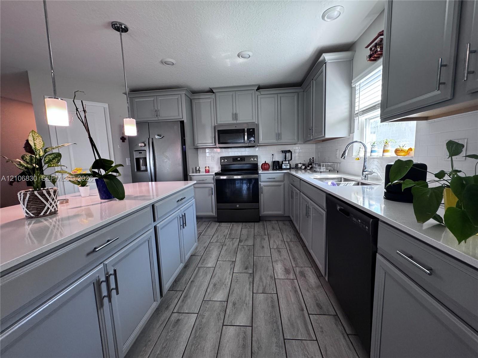 Kitchen featuring gray cabinetry, stone-finish countertops, subway tile backsplash, stainless steel appliances, and wood-finish flooring Kitchen featuring gray cabinetry, stone-finish countertops, subway tile backsplash, stainless steel appliances, and wood-finish flooring