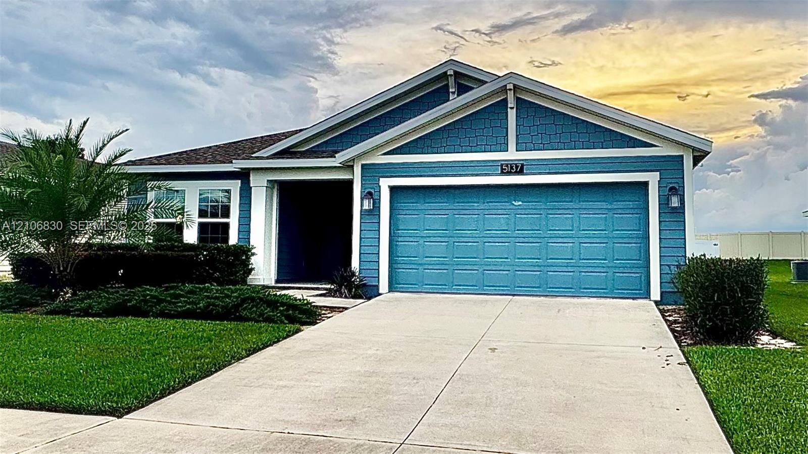 Single-story residence featuring blue horizontal lap siding, shingle-style gable detailing, a two-car garage, and a concrete driveway Single-story residence featuring blue horizontal lap siding, shingle-style gable detailing, a two-car garage, and a concrete driveway