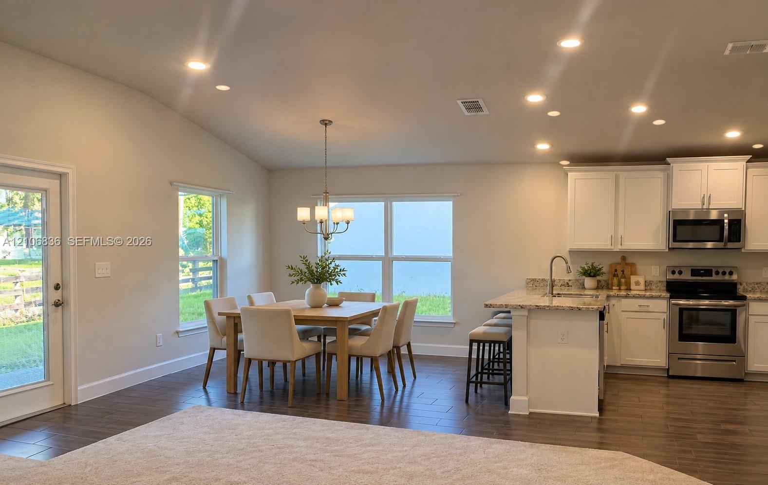 Open-concept kitchen and dining area featuring vaulted ceilings, recessed lighting, wood-finish flooring, white shaker-style cabinetry, and stone-surface countertops Open-concept kitchen and dining area featuring vaulted ceilings, recessed lighting, wood-finish flooring, white shaker-style cabinetry, and stone-surface countertops