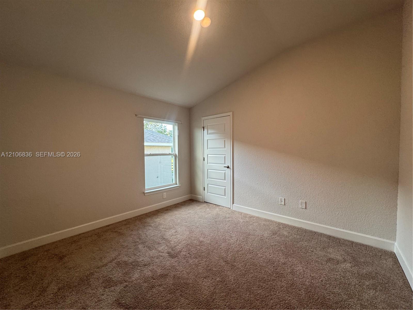 Vaulted ceiling featuring neutral-toned carpeting, five-panel interior door, and single-pane window Vaulted ceiling featuring neutral-toned carpeting, five-panel interior door, and single-pane window