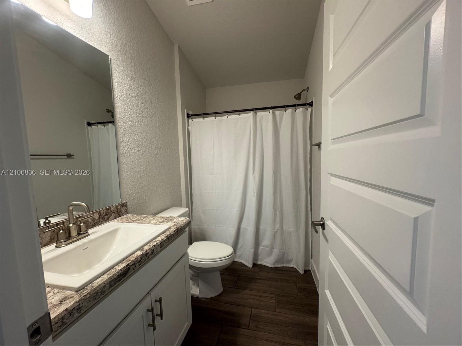 Bathroom featuring a vanity with a white basin and patterned stone-finish countertop, wood-finish flooring, brushed nickel hardware, and a tub-shower combination