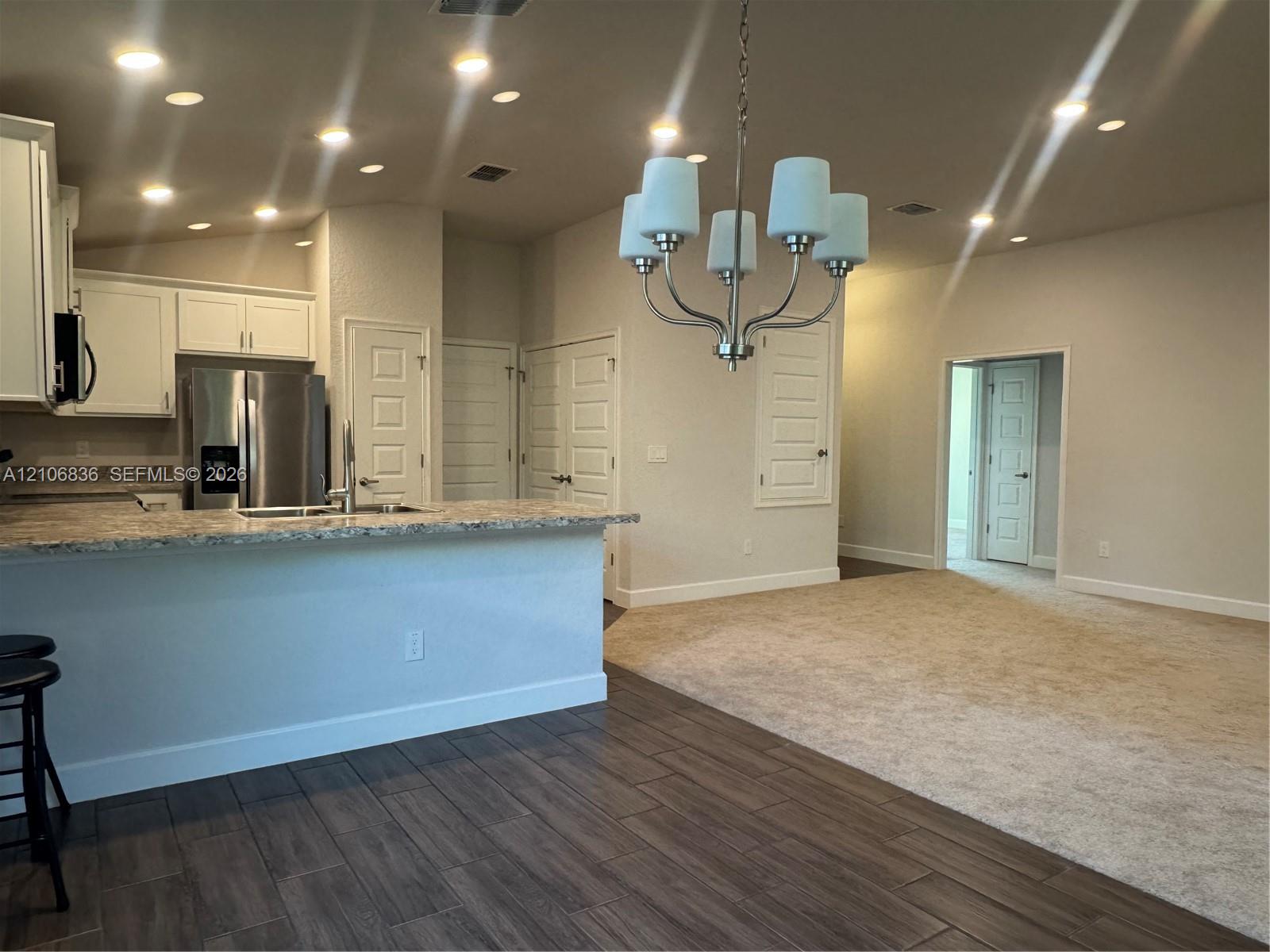 Kitchen featuring white cabinetry, stone-look countertops, stainless steel refrigerator, recessed lighting, and a multi-arm chandelier Kitchen featuring white cabinetry, stone-look countertops, stainless steel refrigerator, recessed lighting, and a multi-arm chandelier