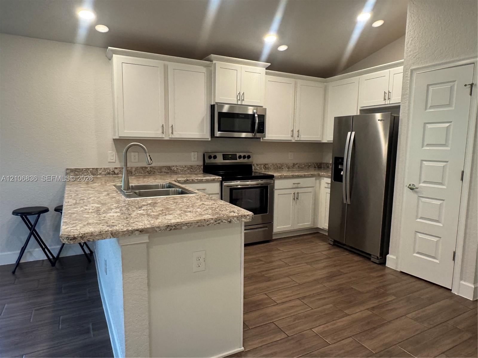 Kitchen featuring white cabinetry, stone-patterned countertops, stainless steel appliances, a high-arc kitchen faucet, and wood-finish tile flooring Kitchen featuring white cabinetry, stone-patterned countertops, stainless steel appliances, a high-arc kitchen faucet, and wood-finish tile flooring
