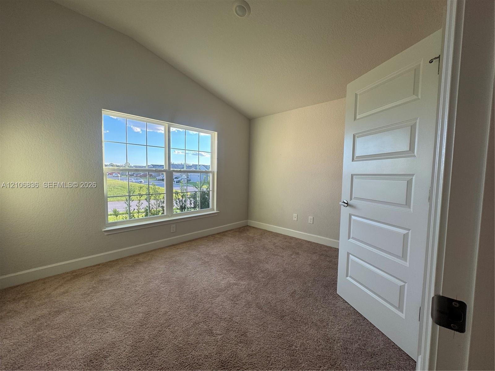 Vaulted ceiling room featuring neutral-toned carpeting, a five-panel interior door, and a multi-pane window