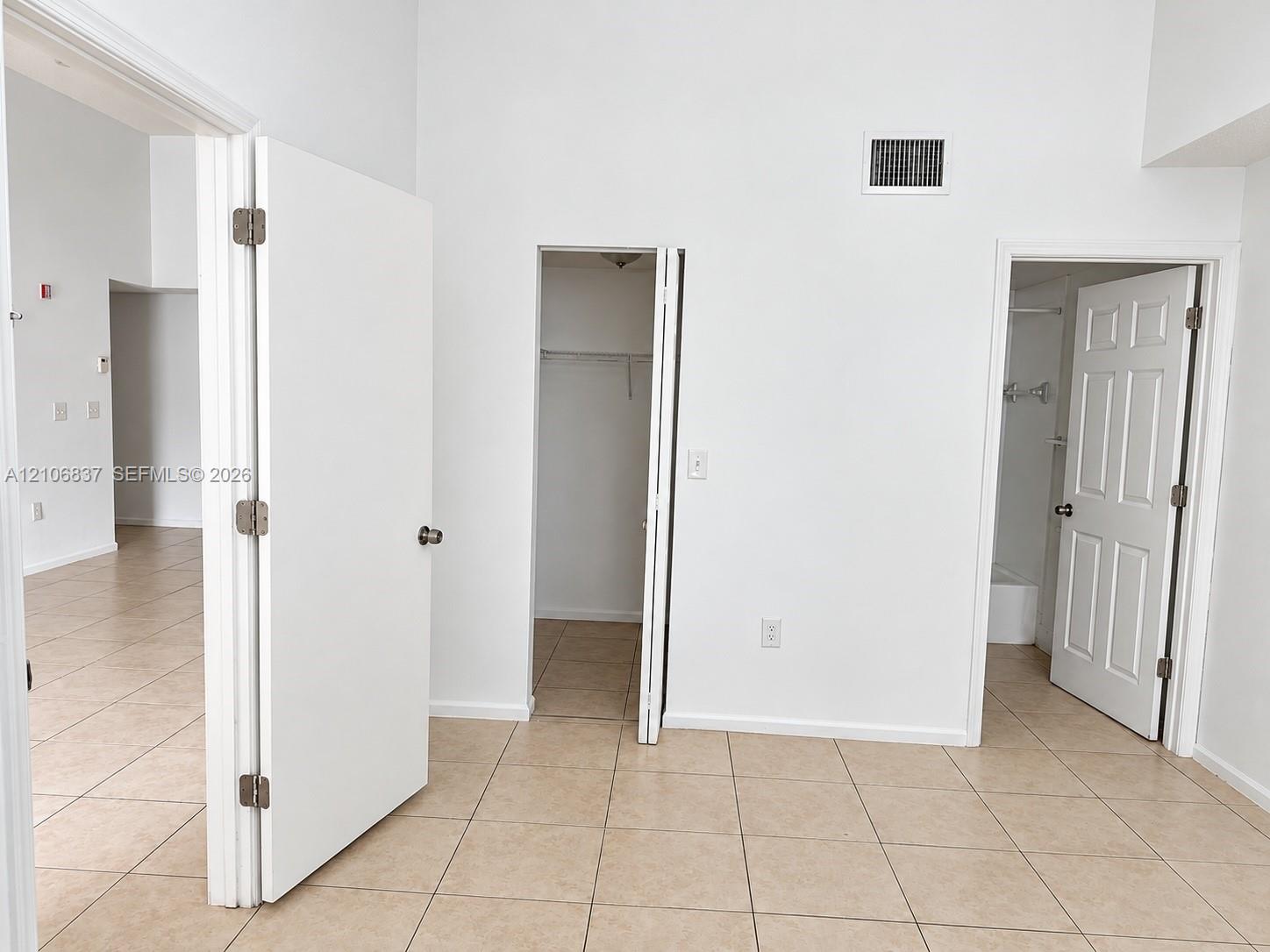 Interior space featuring neutral tile flooring, high ceilings, multiple doorways, and a reach-in closet