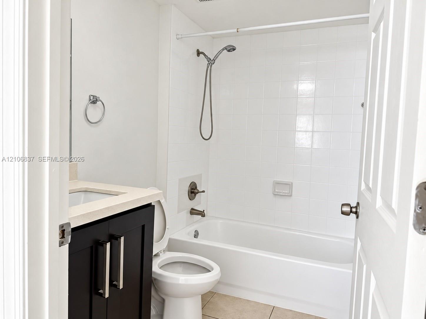 Bathroom featuring a dark wood-finish vanity with a light-toned countertop, a shower and tub combination with tiled surround, and a wall-mounted handheld shower fixture