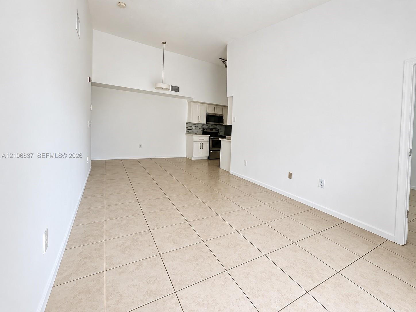 High ceilings with tile flooring and kitchen featuring white cabinetry, stone-finish countertops, and stainless steel appliances