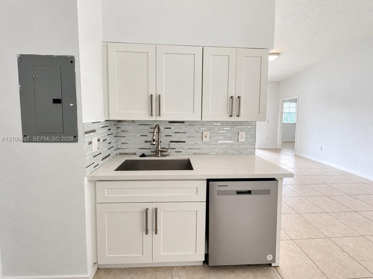 Kitchenette featuring white cabinetry with brushed metal hardware, solid-surface countertops, a stainless steel undermount sink, a mosaic tile backsplash, and an integrated stainless steel dishwasher