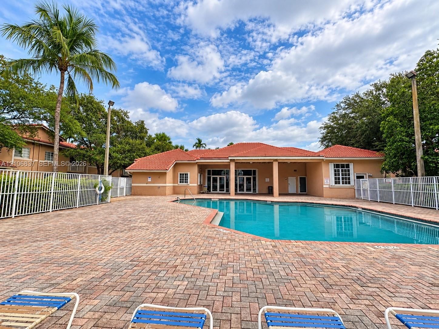 Outdoor swimming pool featuring a brick-paver deck, terracotta tile roofing, and perimeter fencing