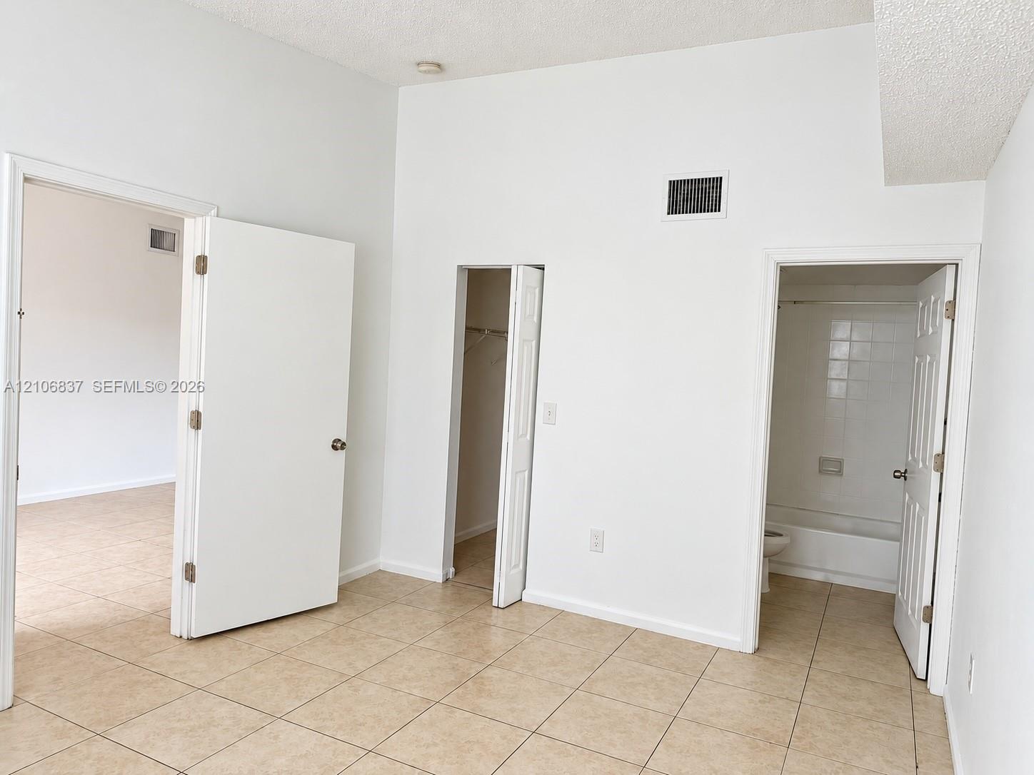 Room featuring tile flooring, vaulted ceilings, and a built-in closet, with access to a bathroom containing a tiled shower-tub enclosure