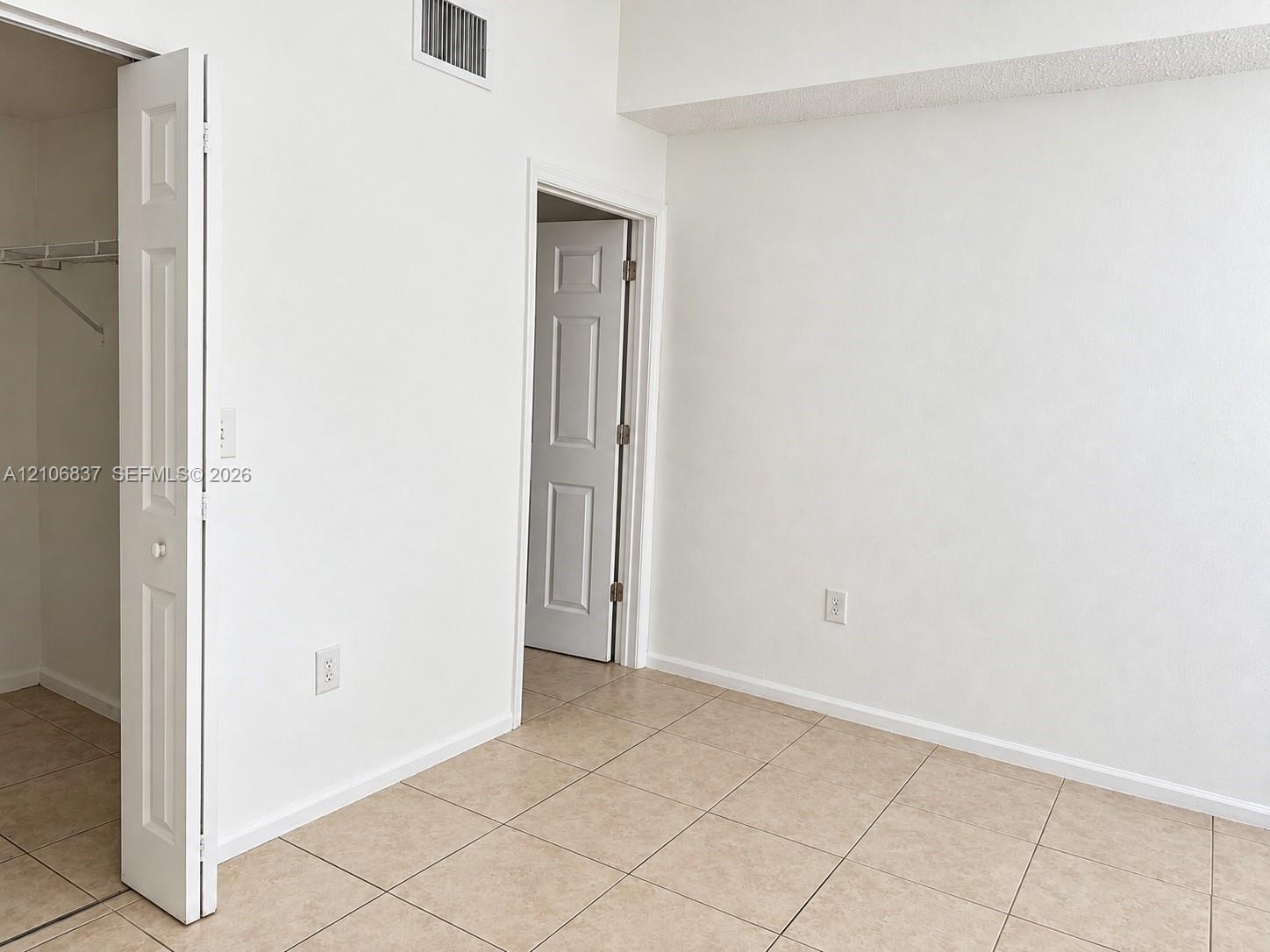 Interior space featuring neutral wall-to-wall tile flooring, white panel doors, and a built-in closet with wire shelving