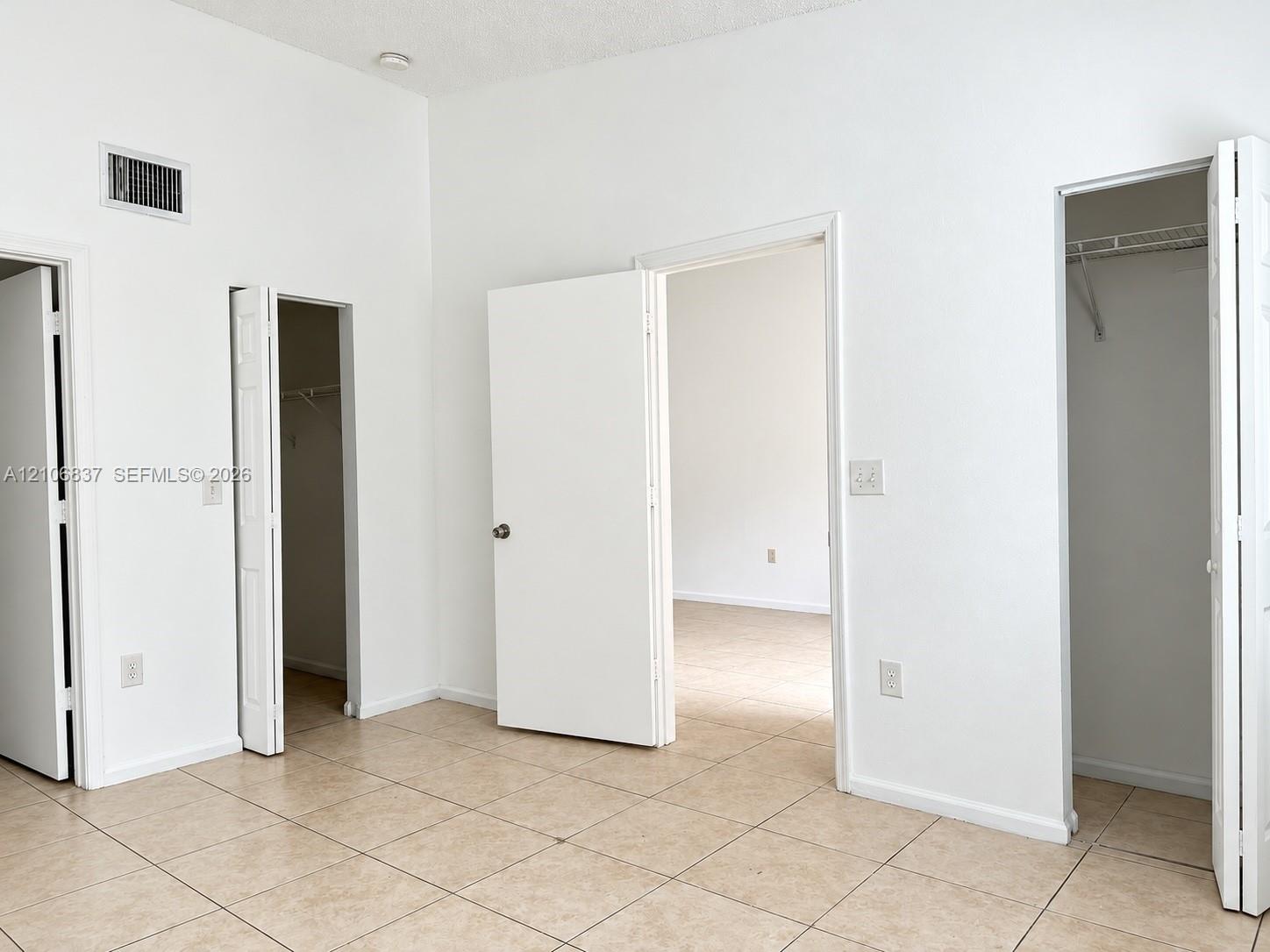 Neutral-toned tile flooring, high ceilings, and multiple closet spaces with interior shelving