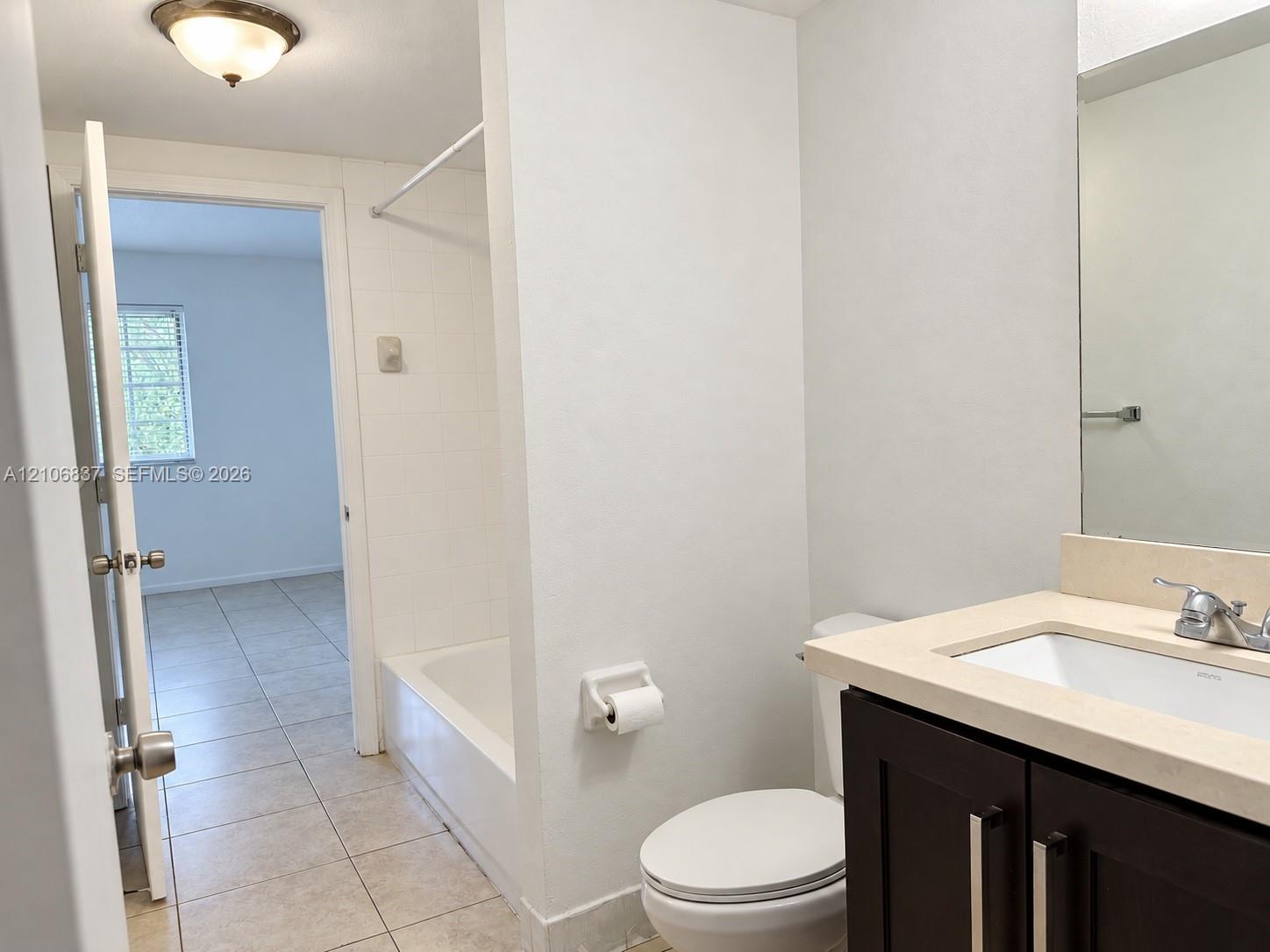 Bathroom featuring a vanity with a light-toned countertop, a tub-shower combination with tiled surround, and ceramic tile flooring